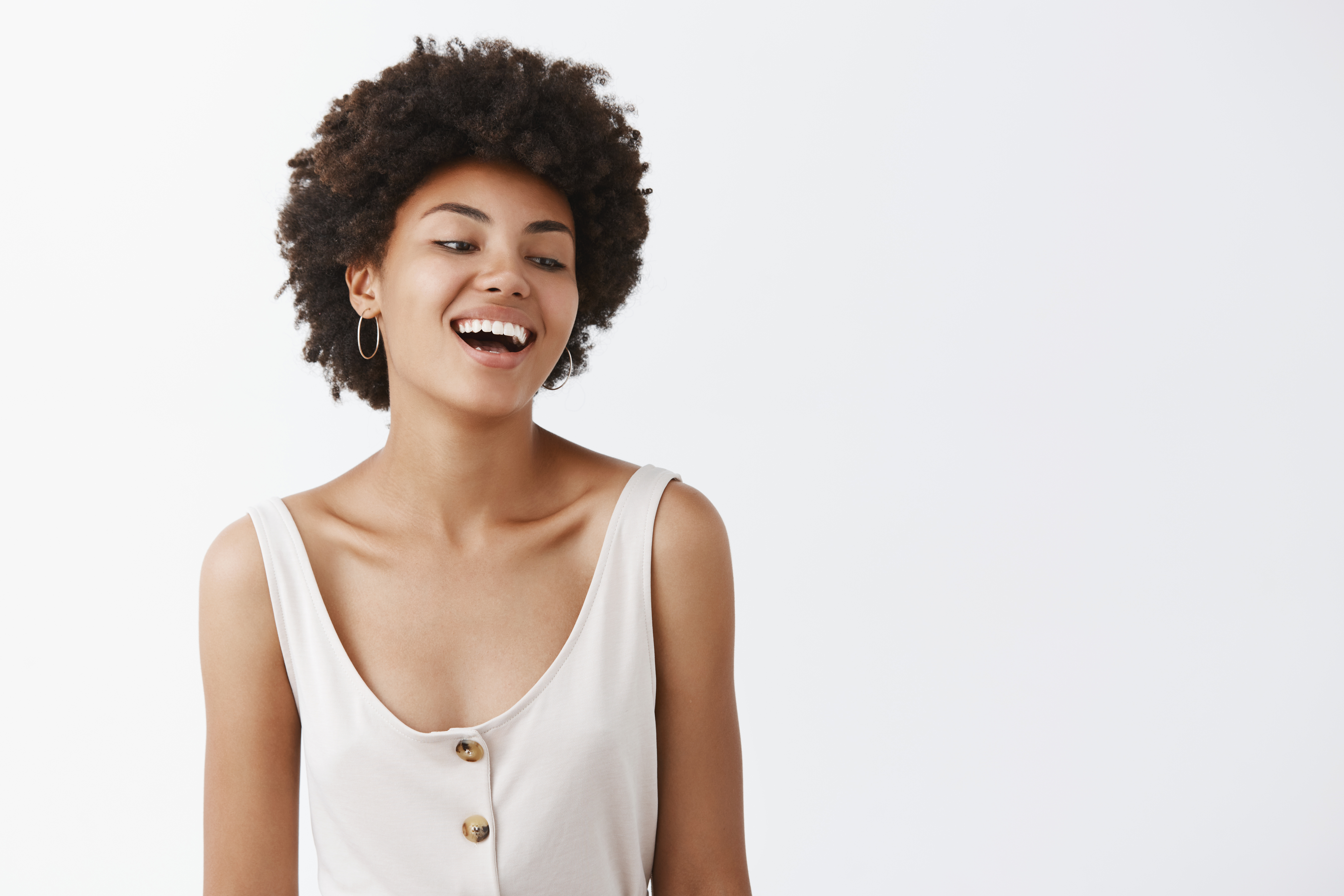 Waist-up shot of carefree emotive and joyful African-American female student with afro hairstyle, laughing out loud and gazing right with amusement and joy, posing over gray background.