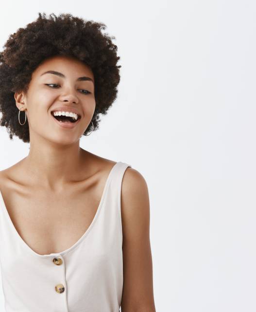 Waist-up shot of carefree emotive and joyful African-American female student with afro hairstyle, laughing out loud and gazing right with amusement and joy, posing over gray background.